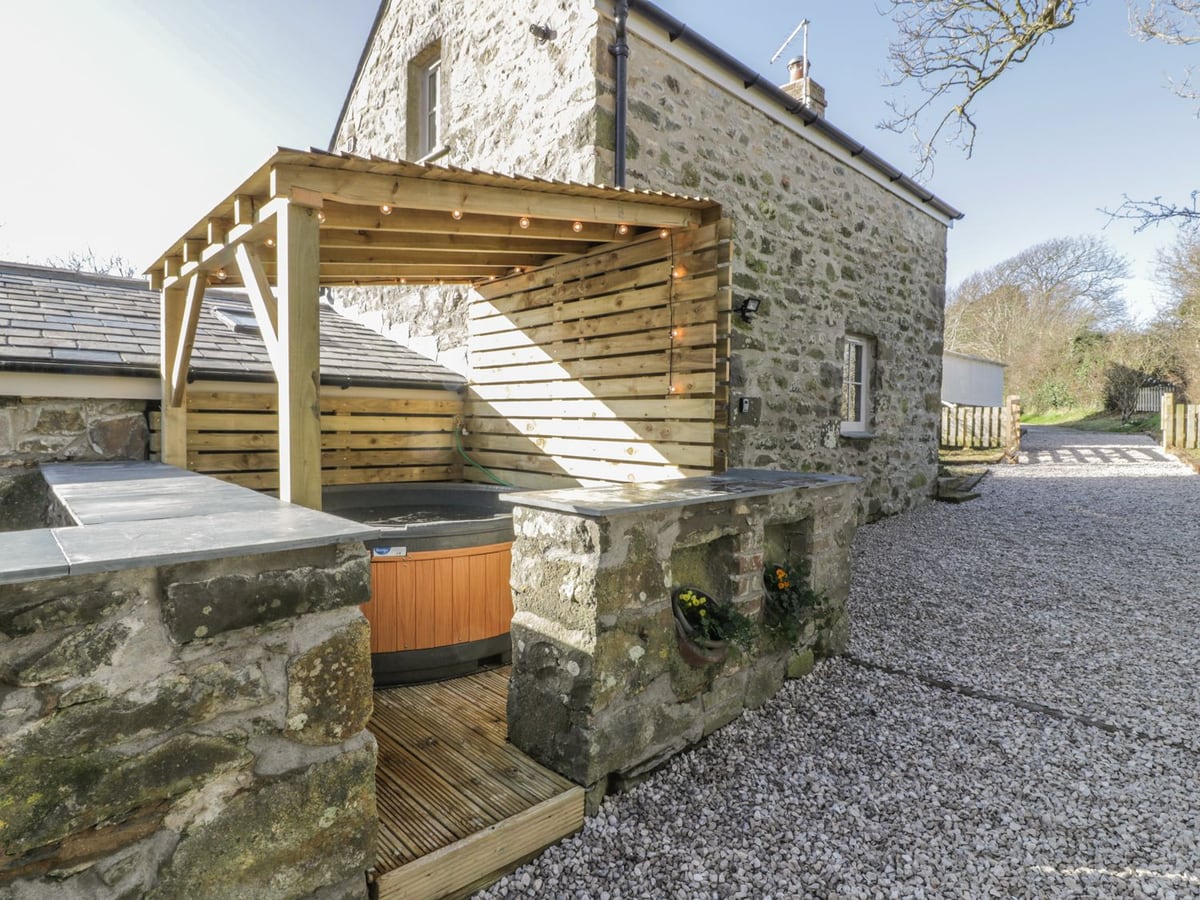 Owl Cottage stone walls and a hot tub under a timber canopy with string lights beside a gravel path