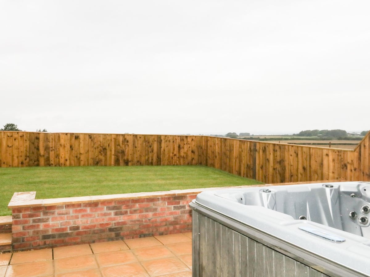 Hot tub beside a paved patio, raised lawn and timber garden fencing at Owl View