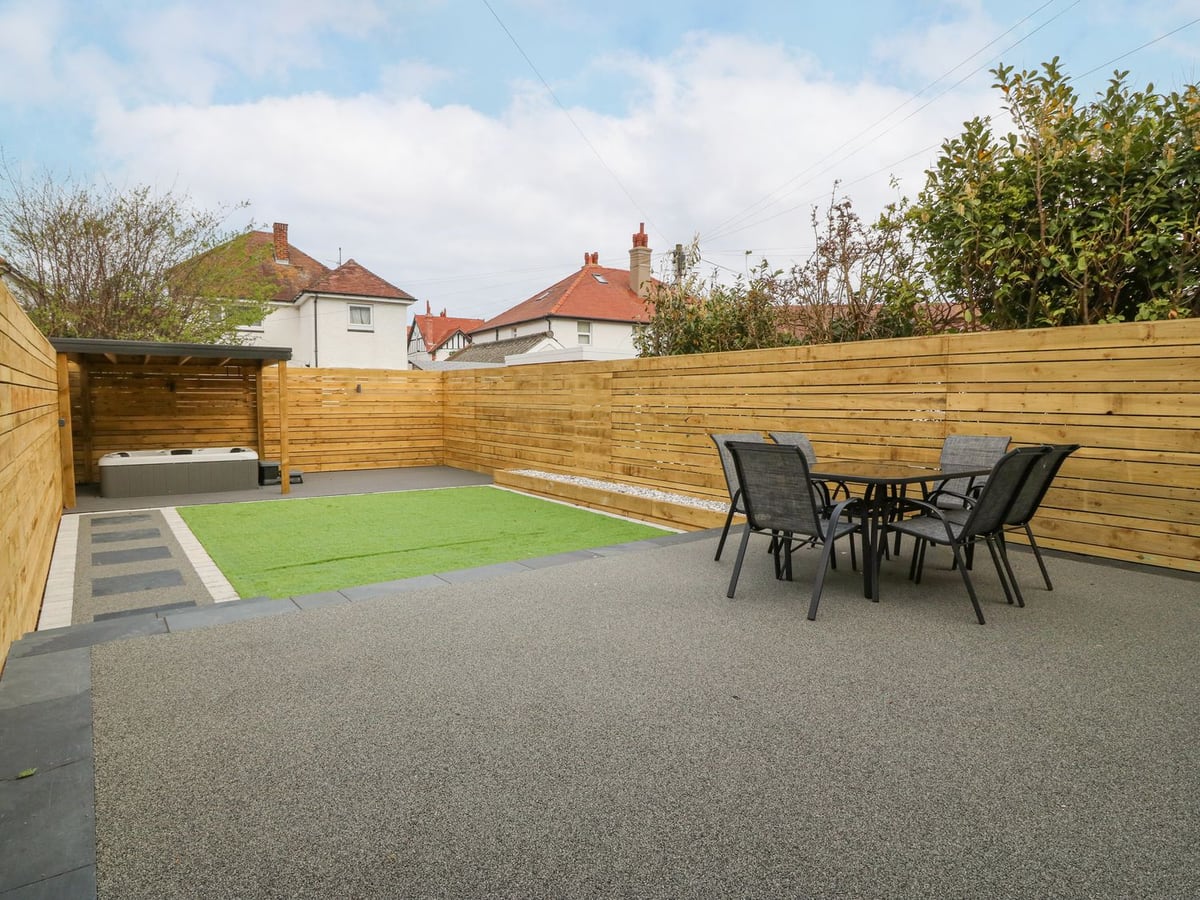 Fenced rear garden at Park View with artificial lawn, patio table and chairs and a hot tub under a shelter