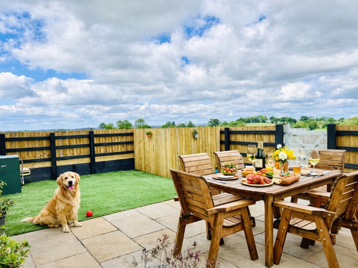 Golden dog beside a patio dining table and timber fence in the garden at Pastures Barn.