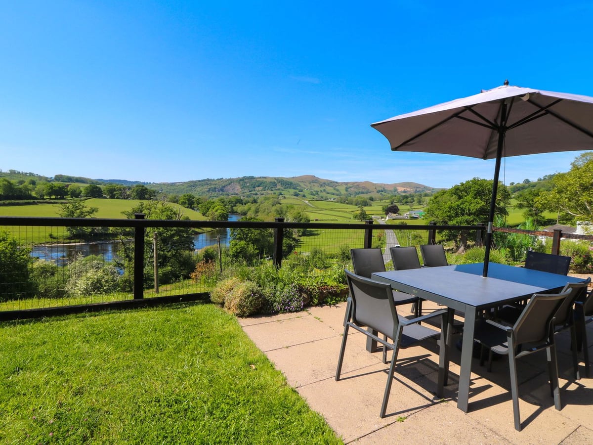Patio dining table and parasol beside a lawn and railing above a river valley at Pen Y Banc