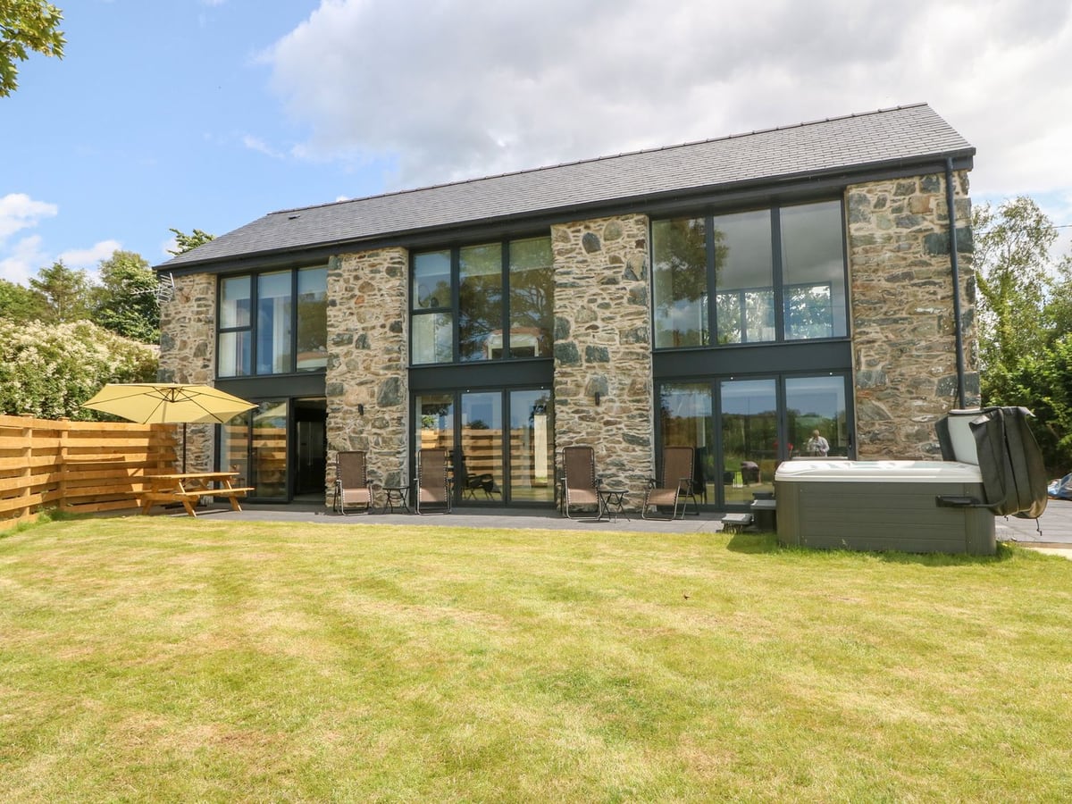 Pen Y Bryn stone-and-glass exterior with lawn, outdoor chairs and a hot tub beside the house