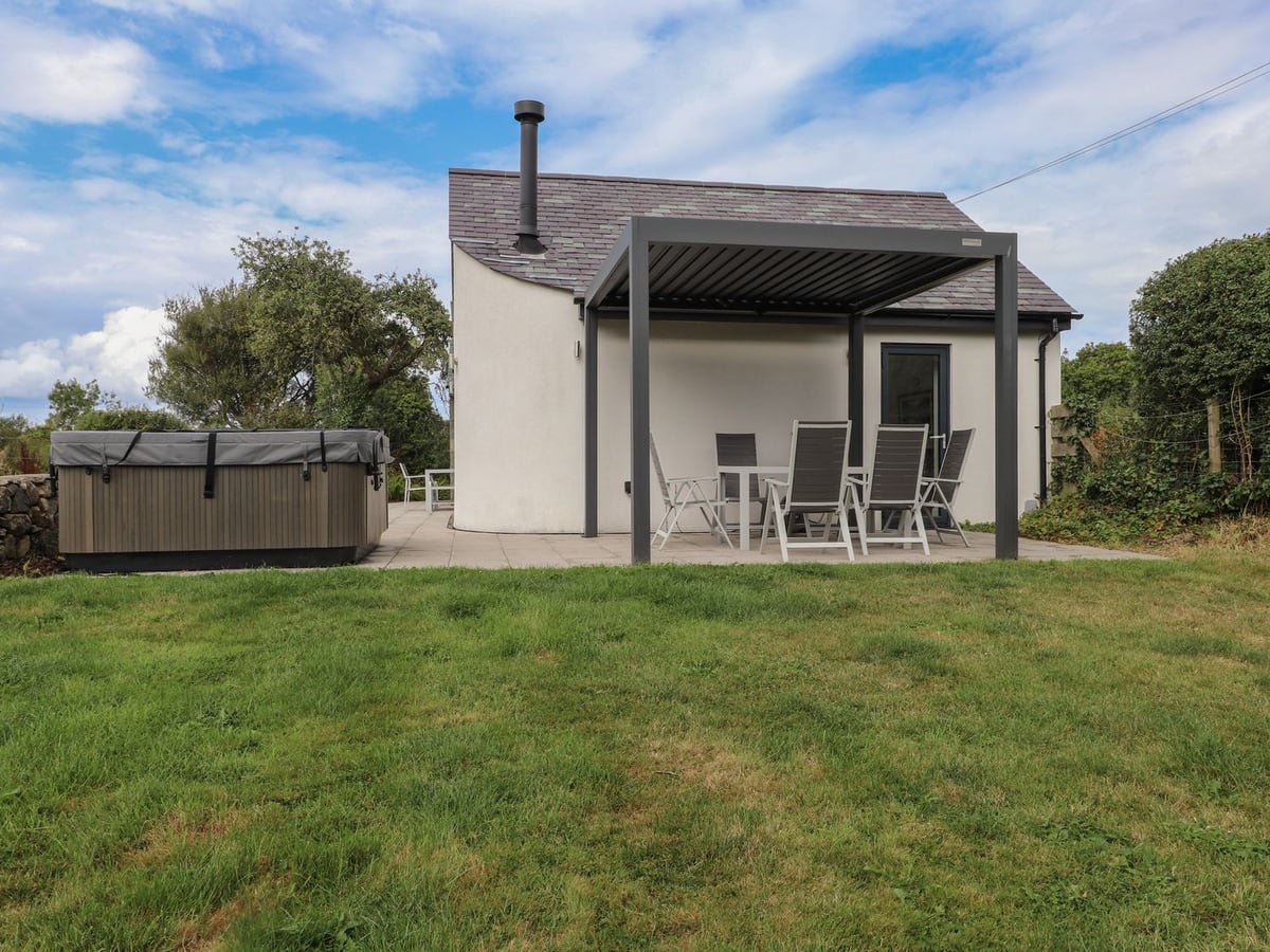 Pen Y Cefn lawn and white cottage with pergola patio dining and a hot tub with its lid on