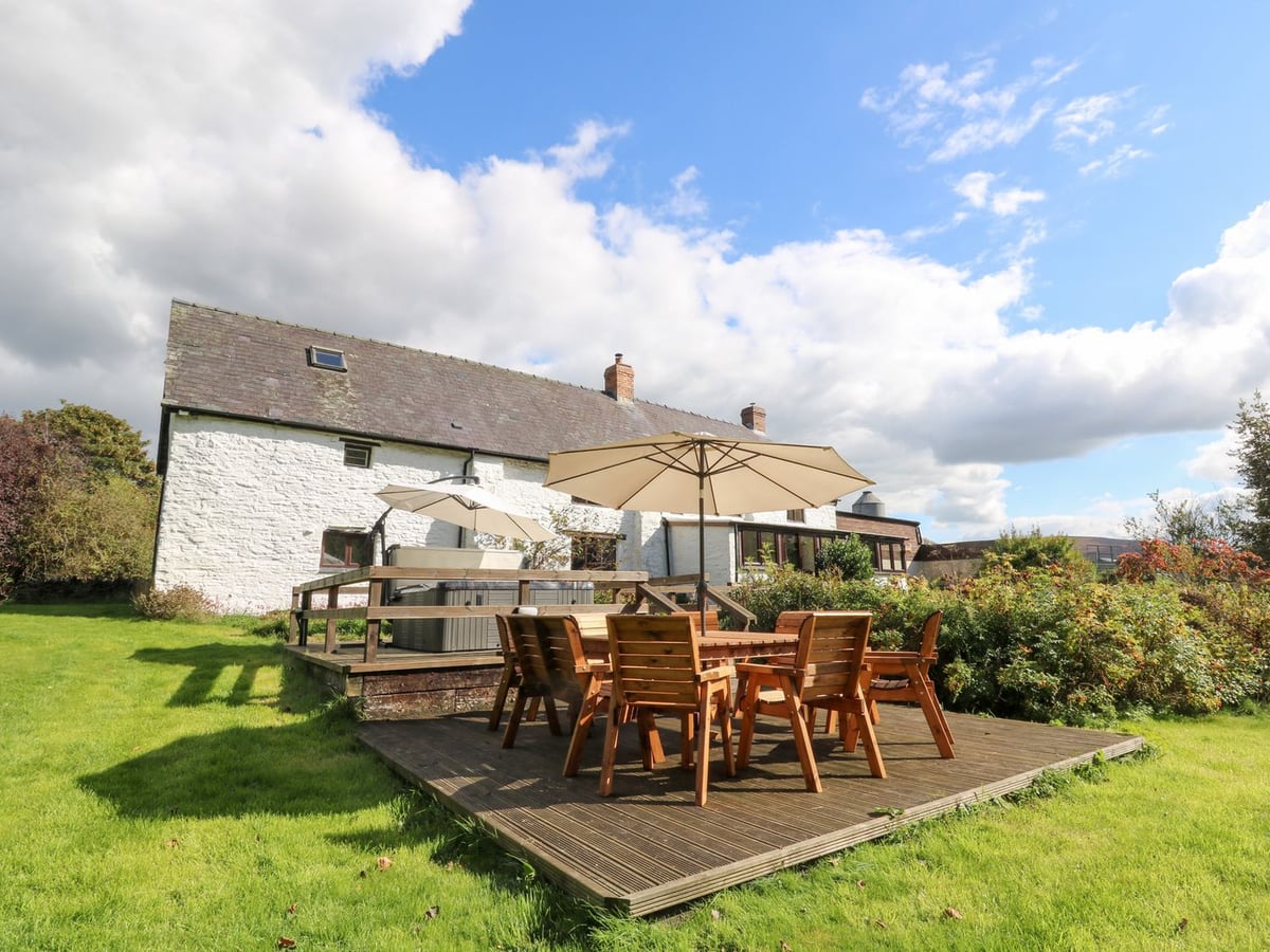 Penarth white stone farmhouse with lawn, decked dining area under a parasol and raised hot tub deck