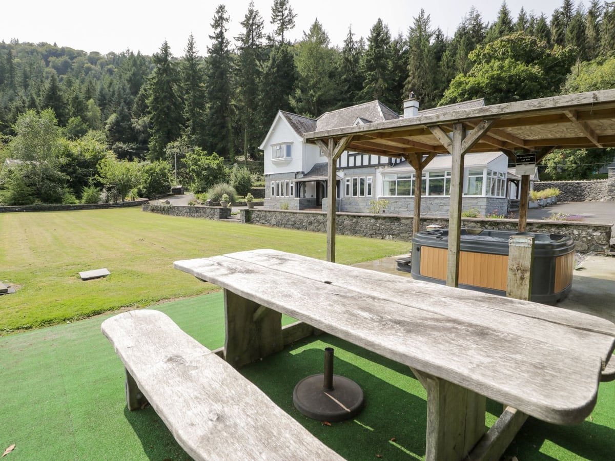 Pengwern picnic table on artificial turf by a hot tub under a timber shelter, with lawn and house behind