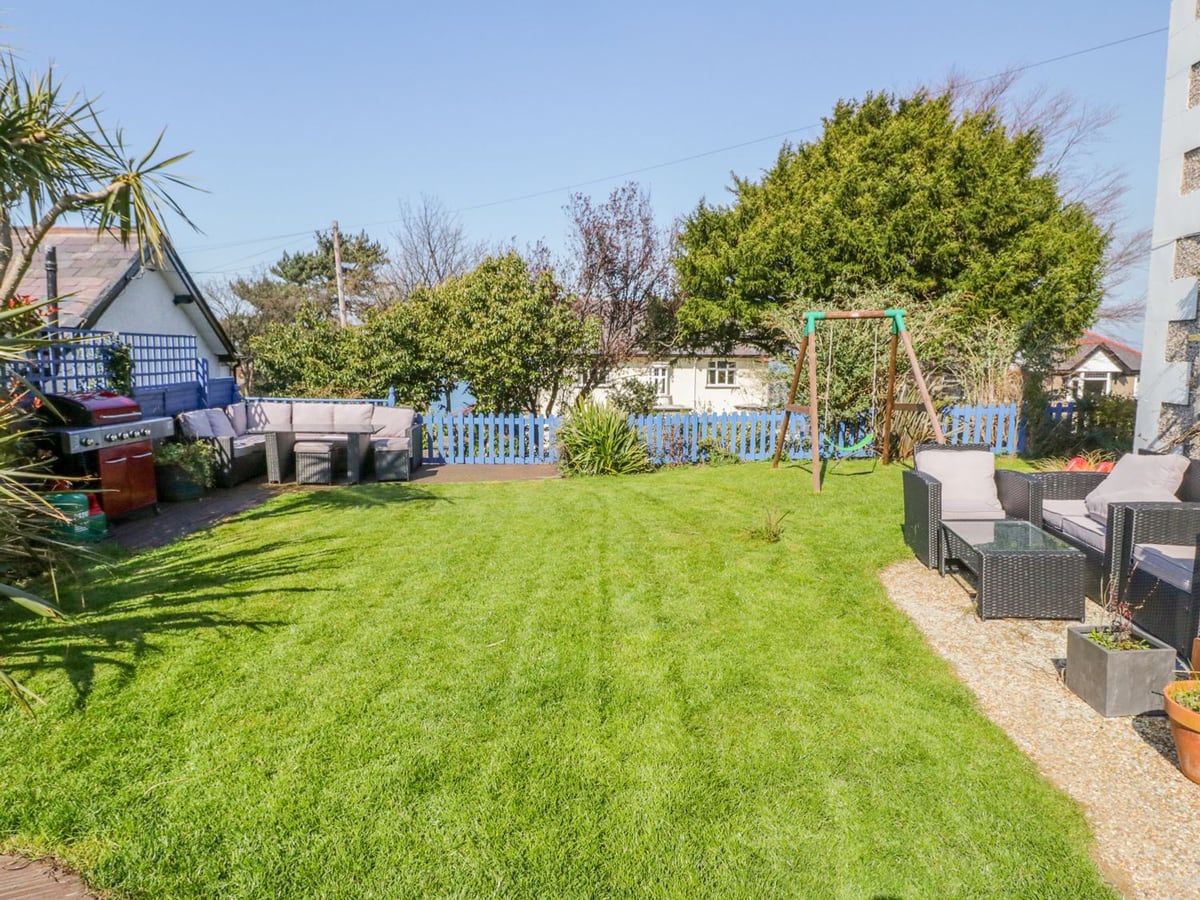 Penholm lawn garden with outdoor seating, barbecue, blue fence, and swing