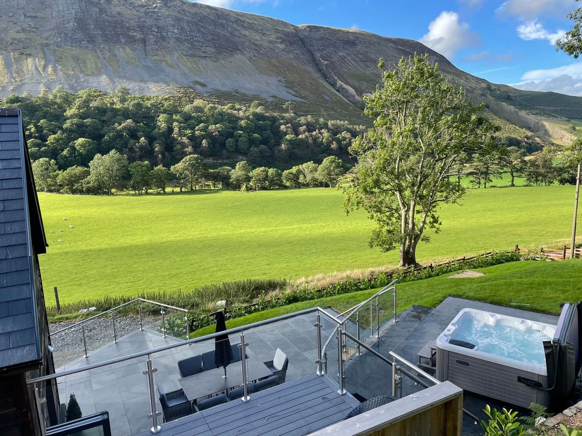Hot tub and patio dining terrace at Pennant Uchaf, with lawn, fields and a steep valley hillside beyond