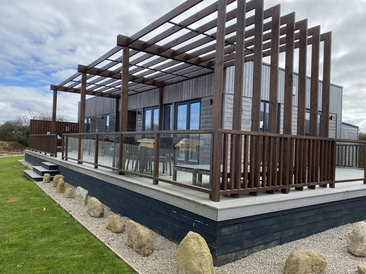 Pentewan - 67's timber exterior, raised deck and pergola beside a lawn edged with large stones