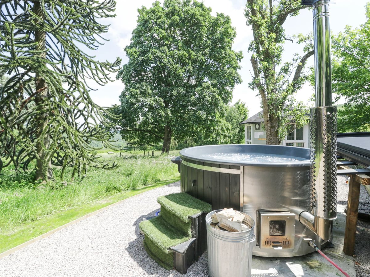 Round outdoor hot tub on gravel at Pentre Hall, beside lawn, trees and a summerhouse