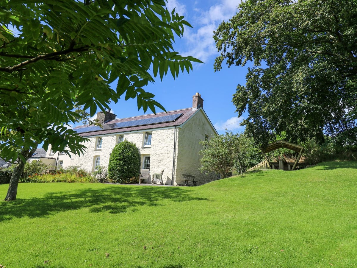 Penuwch Fach white farmhouse beside a broad green lawn, mature trees and a timber garden seat