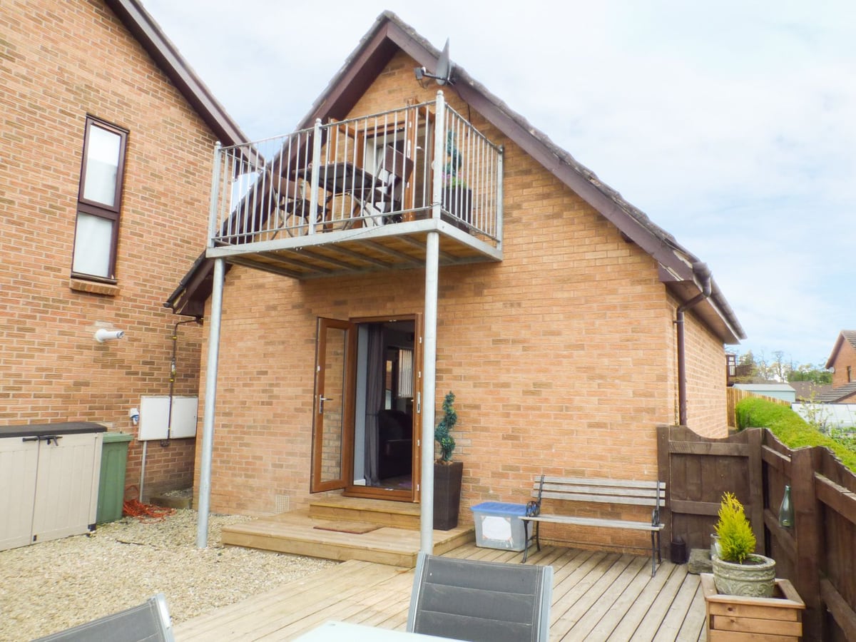 Penylodge brick lodge with upstairs balcony, open ground-floor doors, timber deck, bench and side fence