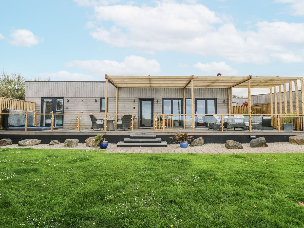 Petroc's timber exterior and deck with a pergola, outdoor seating and steps down to a lawn