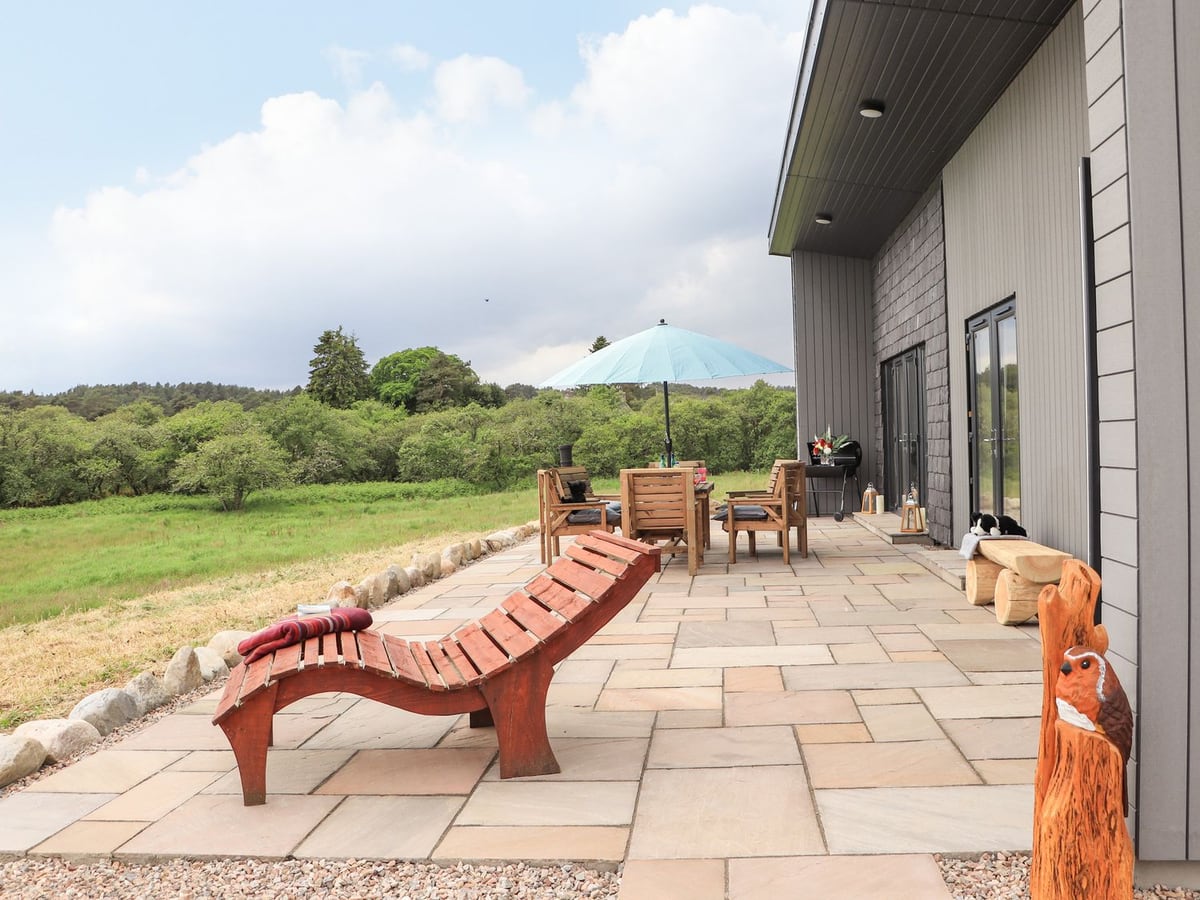 Pine Marten terrace with wooden loungers, a dining table and open grassland beside the lodge