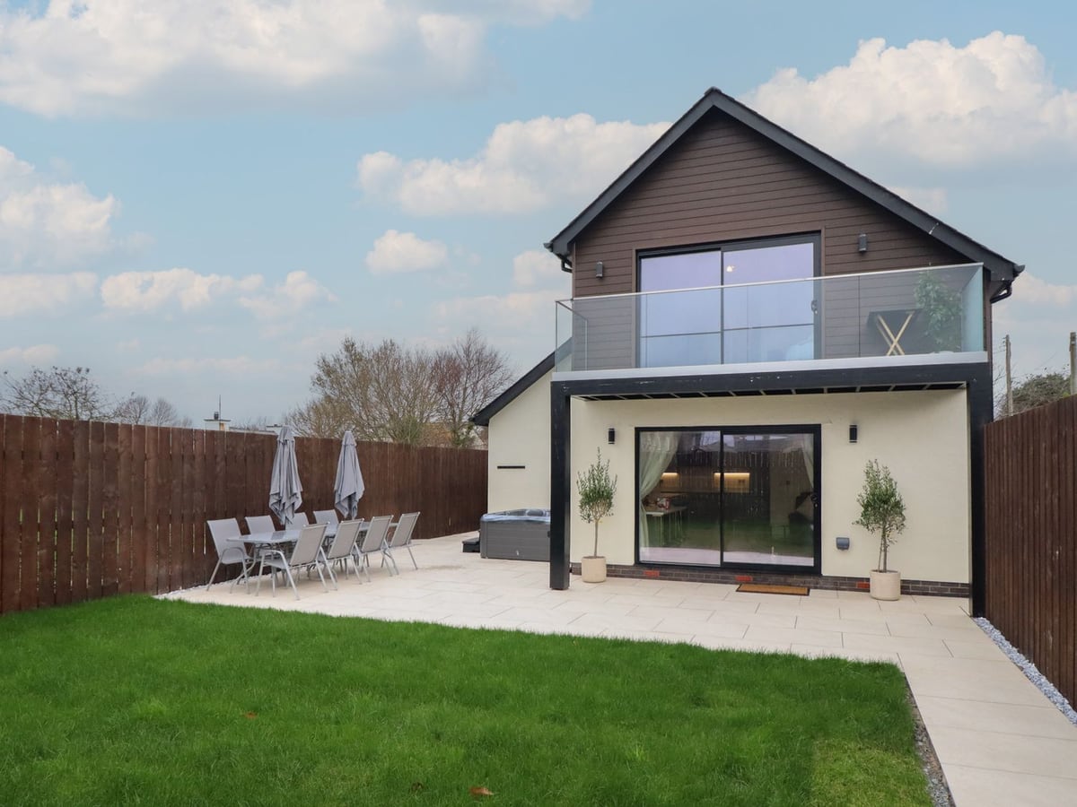 Pistyll Ddu rear gable with balcony, lawn and patio dining chairs beside the house