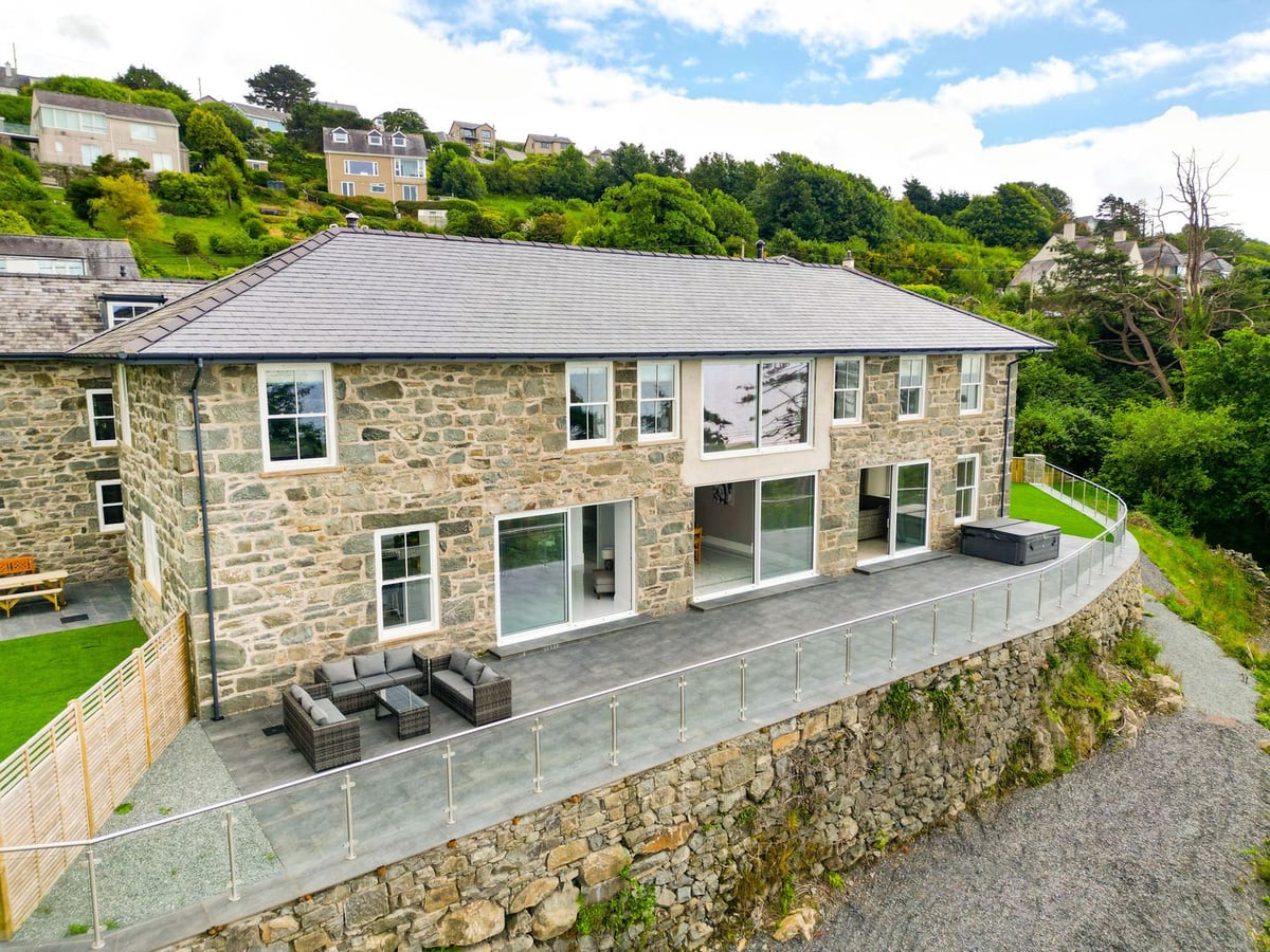 Plas Amherst stone exterior with terrace seating, hot tub, and hillside backdrop