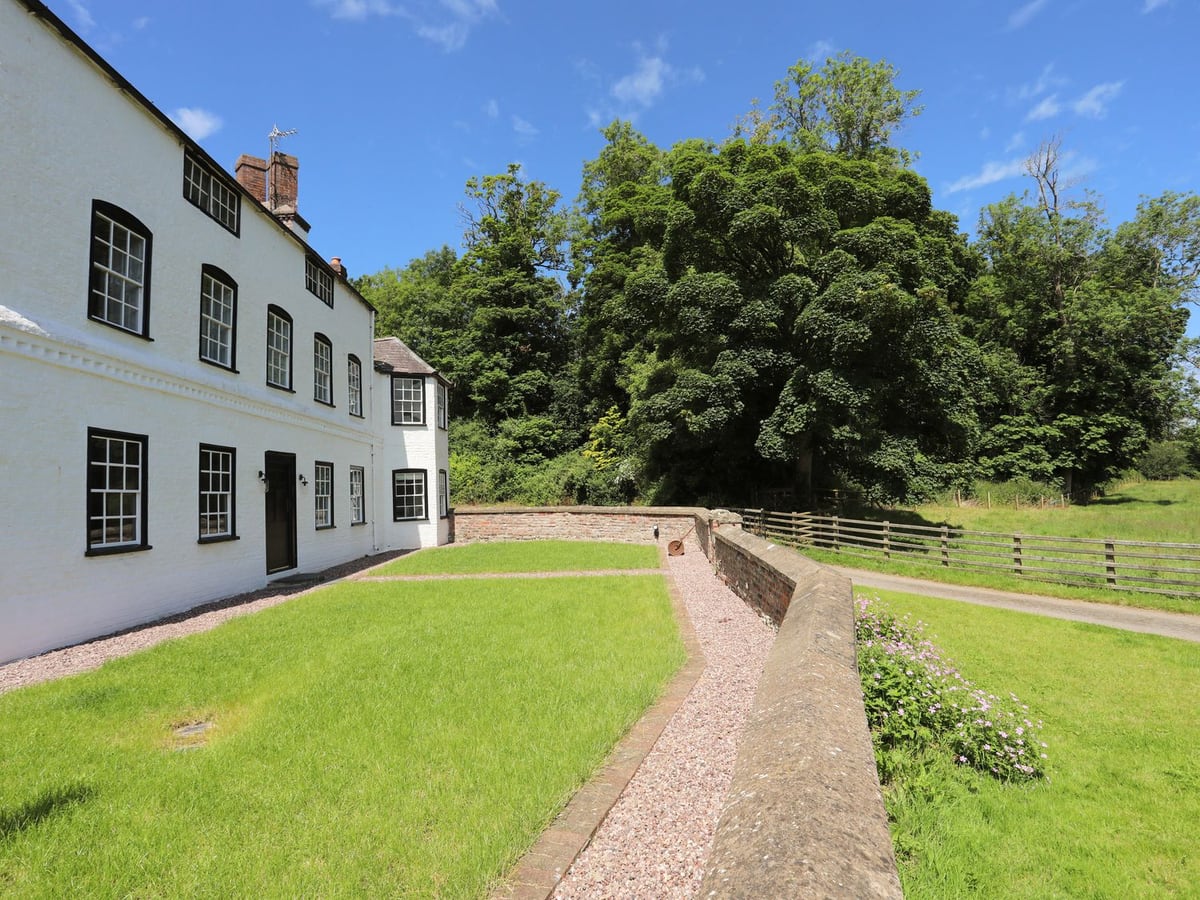 Plas Coch white farmhouse with a walled front lawn, gravel path and fenced fields and trees