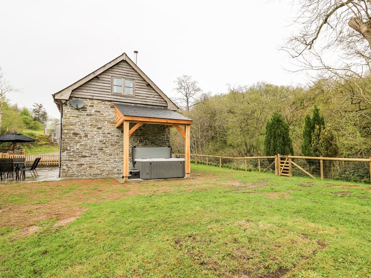 Ploony Barn stone and timber gable with a covered hot tub, lawn and post and wire fence with gate