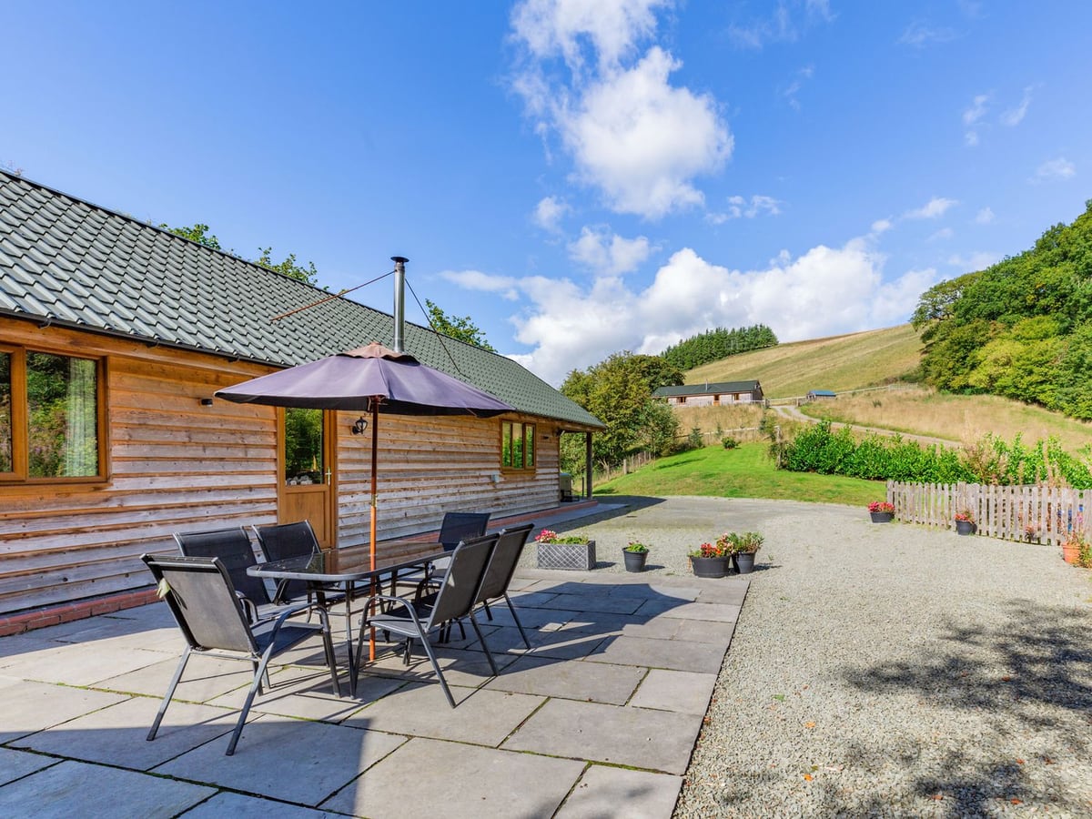Ploony Hill Lodge timber lodge with patio table and parasol, lawn and hillside with another lodge