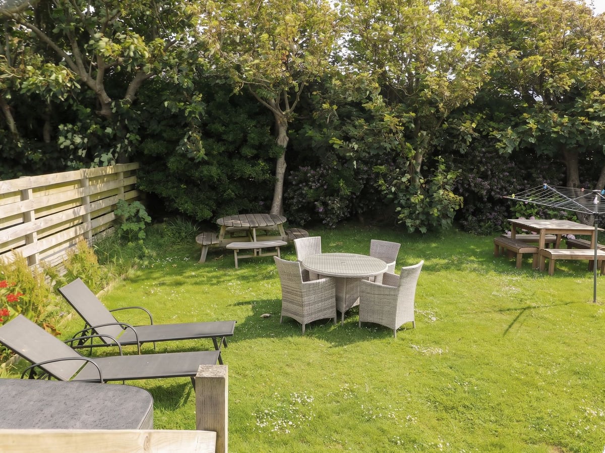 Rear lawn at Porth Ewyn with a wicker dining set, picnic tables, sun loungers and a timber fence