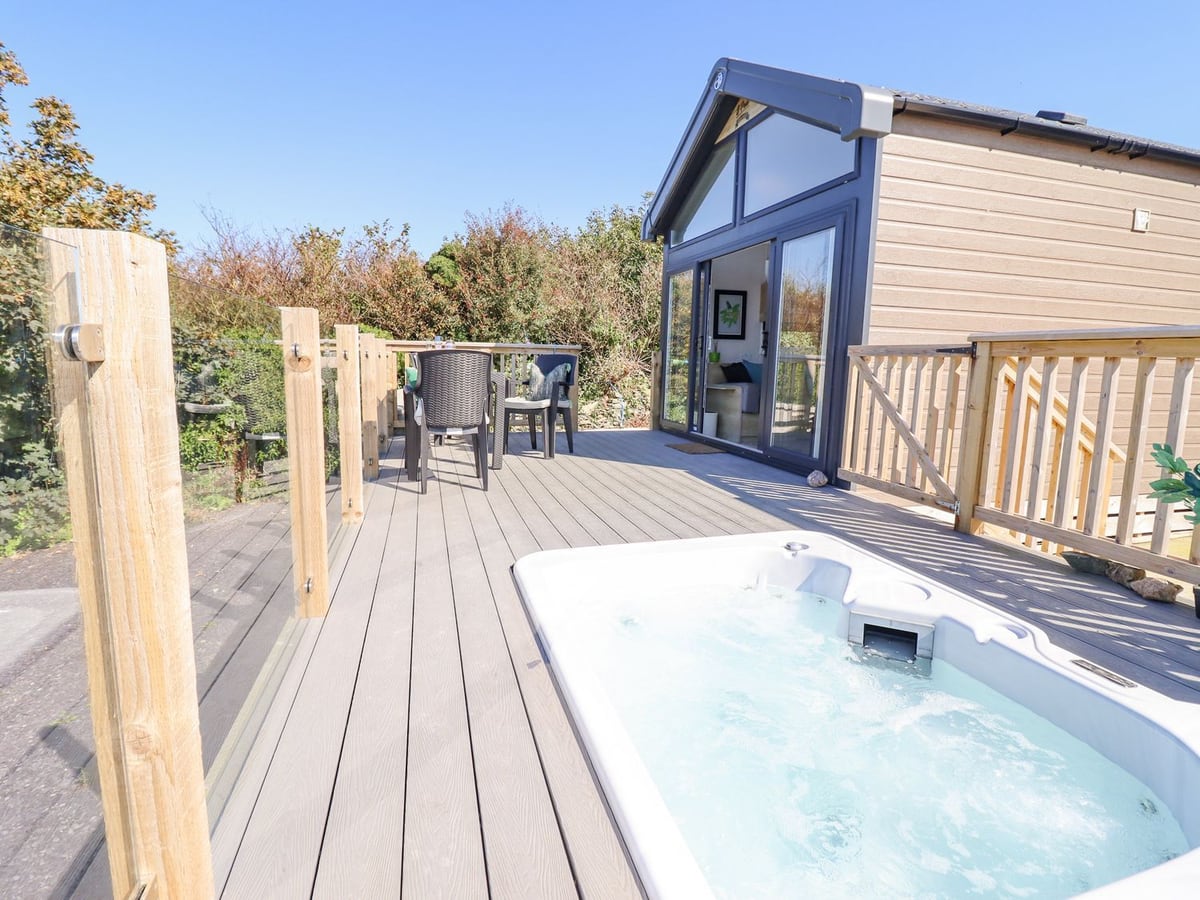 Posh Pod glazed front with a sunken hot tub, table and chairs on a deck with glass and timber rails