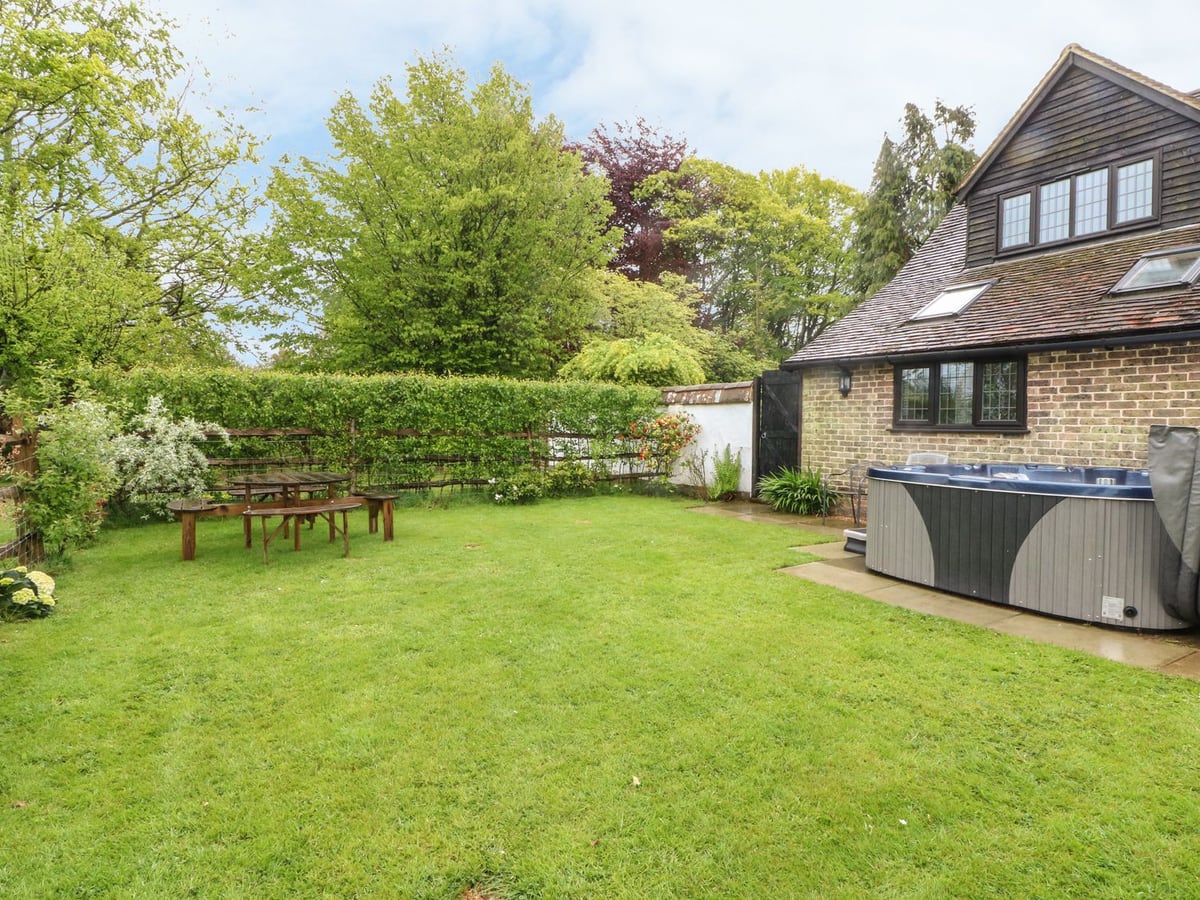 Pump House beside its lawn, outdoor hot tub and picnic table, with trees along the boundary