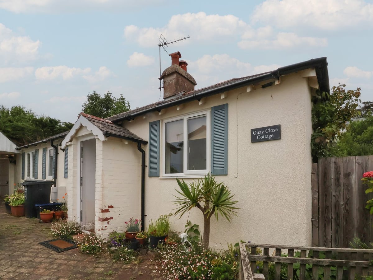 Cream cottage with blue shutters, entrance porch and potted plants at Quay Close Cottage