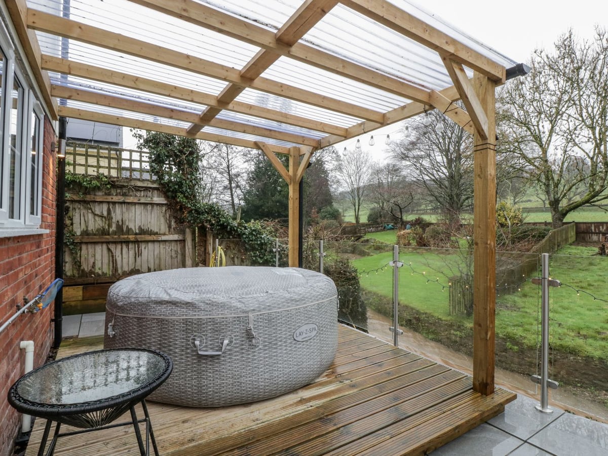 Covered hot tub on Ranbir House decking, with a glass railing overlooking the garden and stream