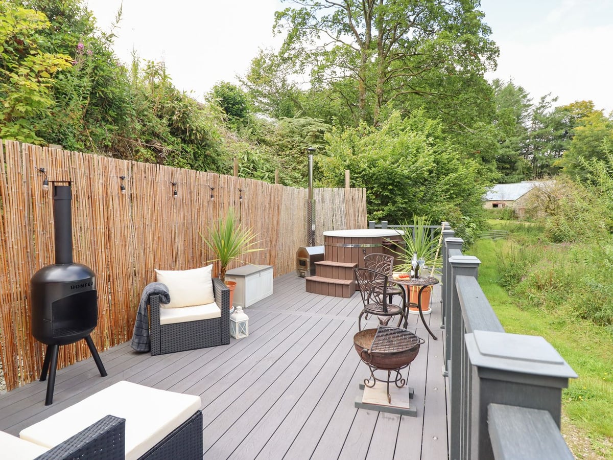 Railed deck at Red Kite with a wood-fired hot tub with its lid on, chiminea, fire pit and bistro set