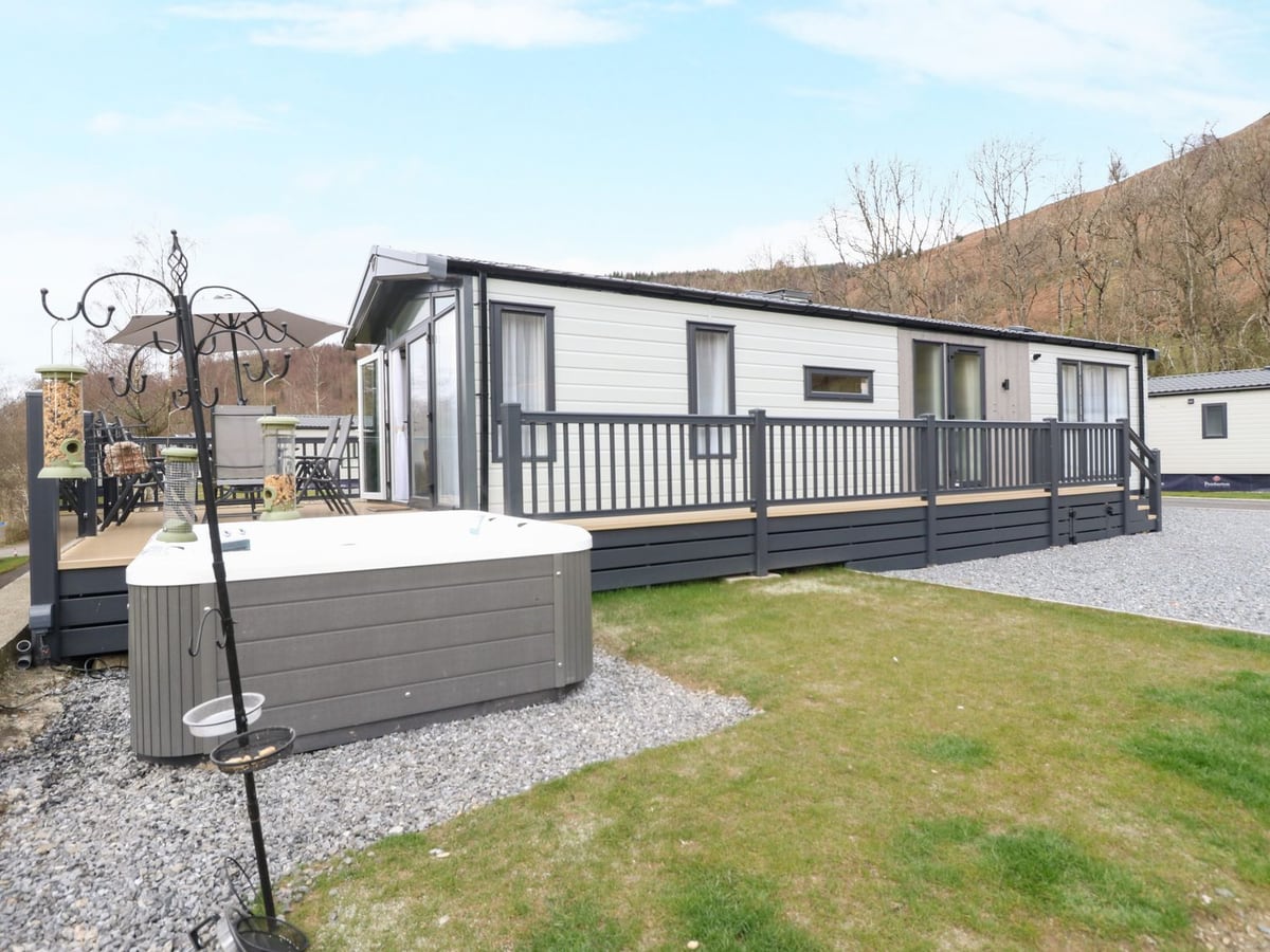 Red Kite Lodge with a railed deck, hot tub and small lawn, with another lodge visible nearby