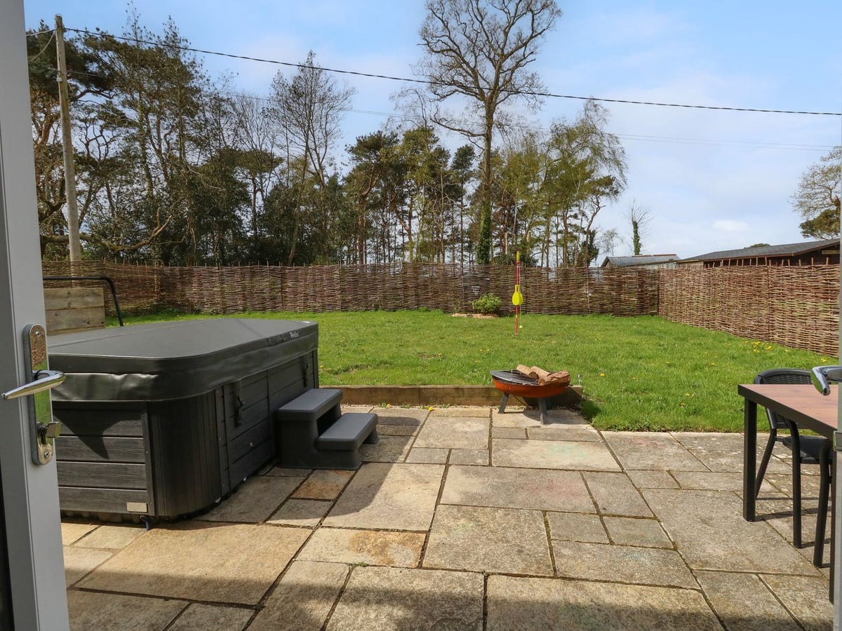 Covered hot tub, paved patio and lawn behind a woven fence at Rempstone Farmhouse