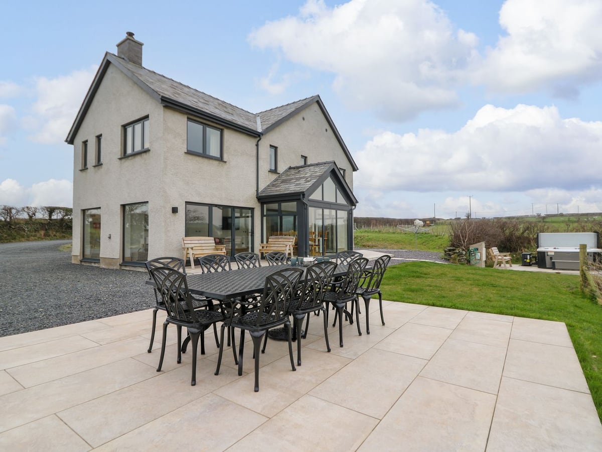Rhandir Hen with a paved patio dining table, lawn and a hot tub at the side, with fields beyond