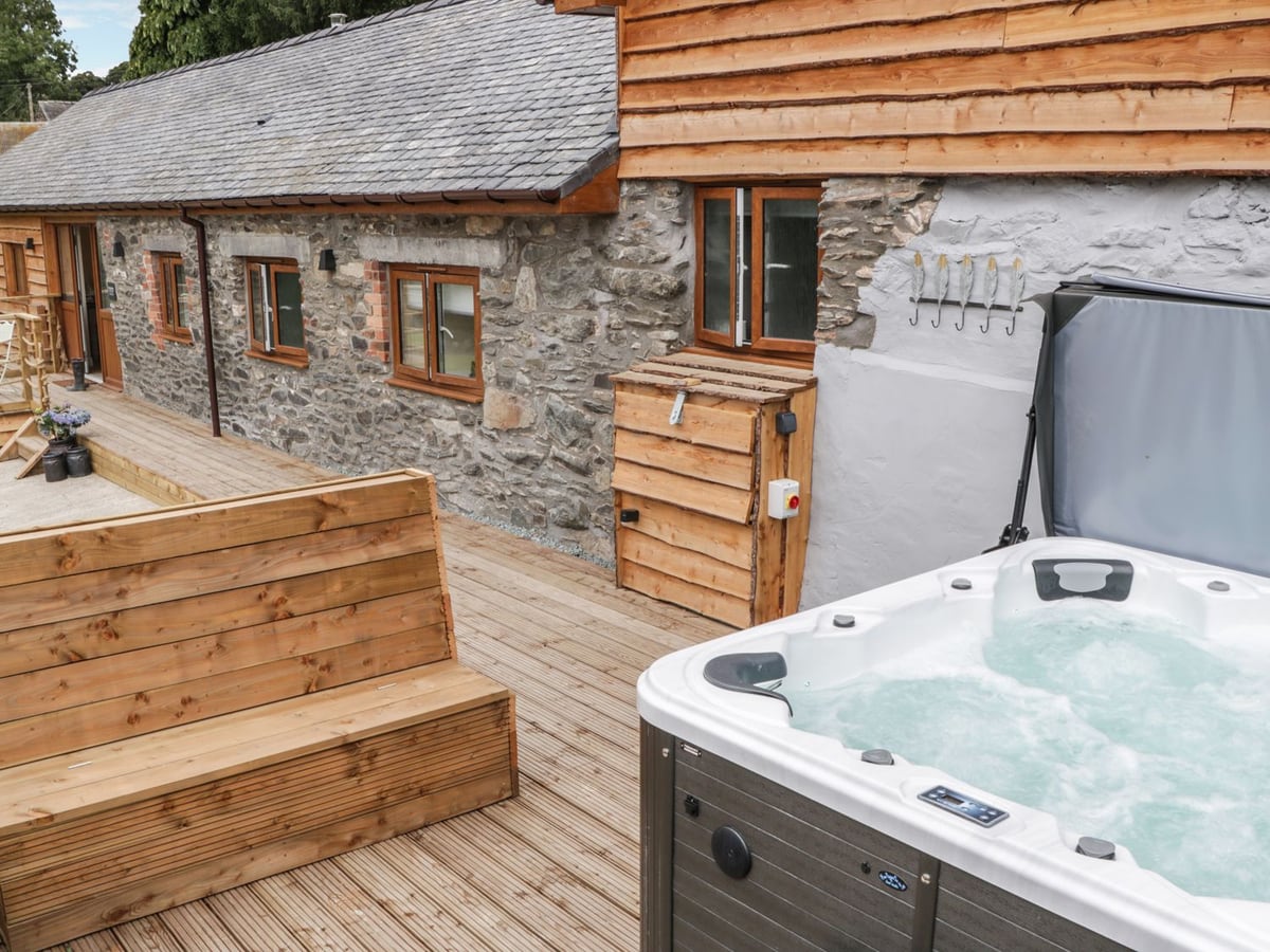 Hot tub on a timber deck beside the stone and timber-clad barn at Rhianwen, with a wooden bench
