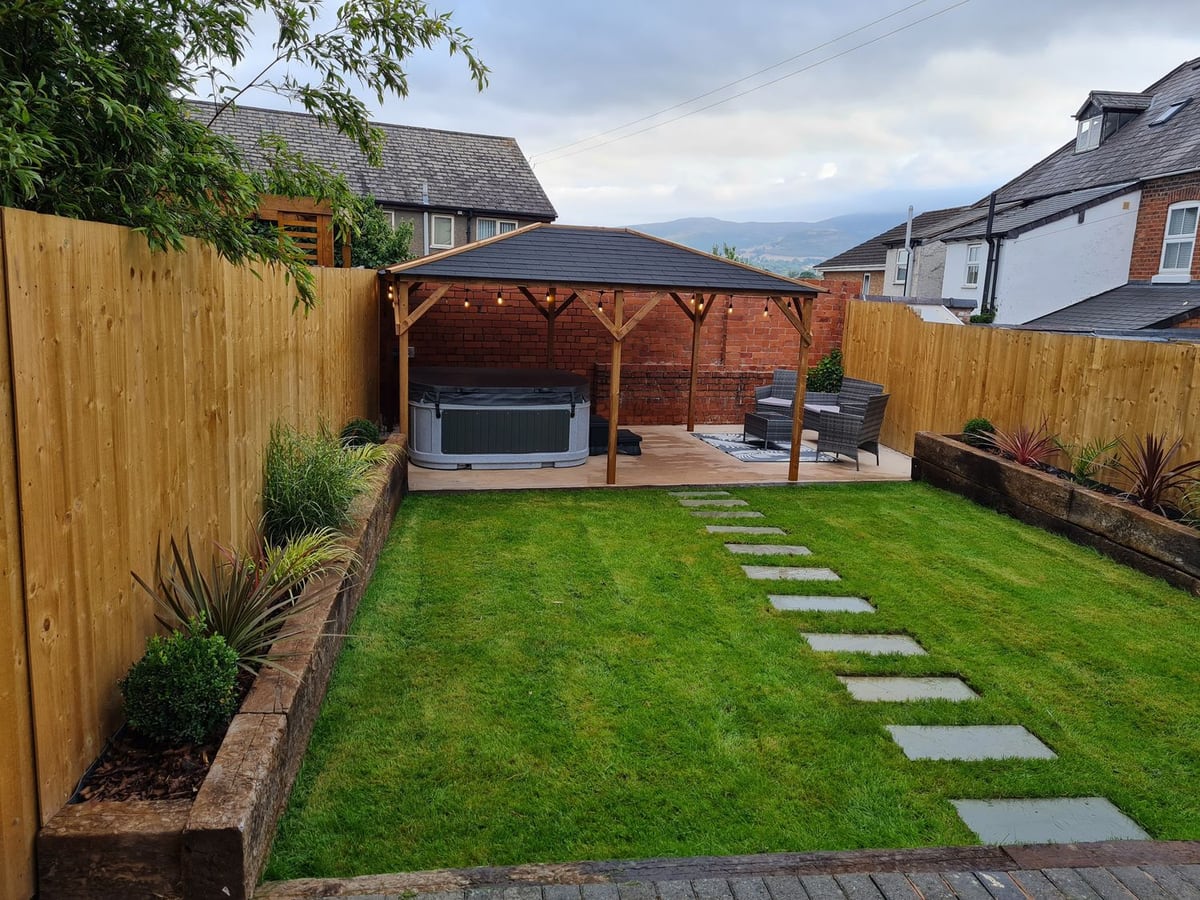Rhif Saith fenced rear lawn with stepping stones leading to a hot tub and seating under a gazebo