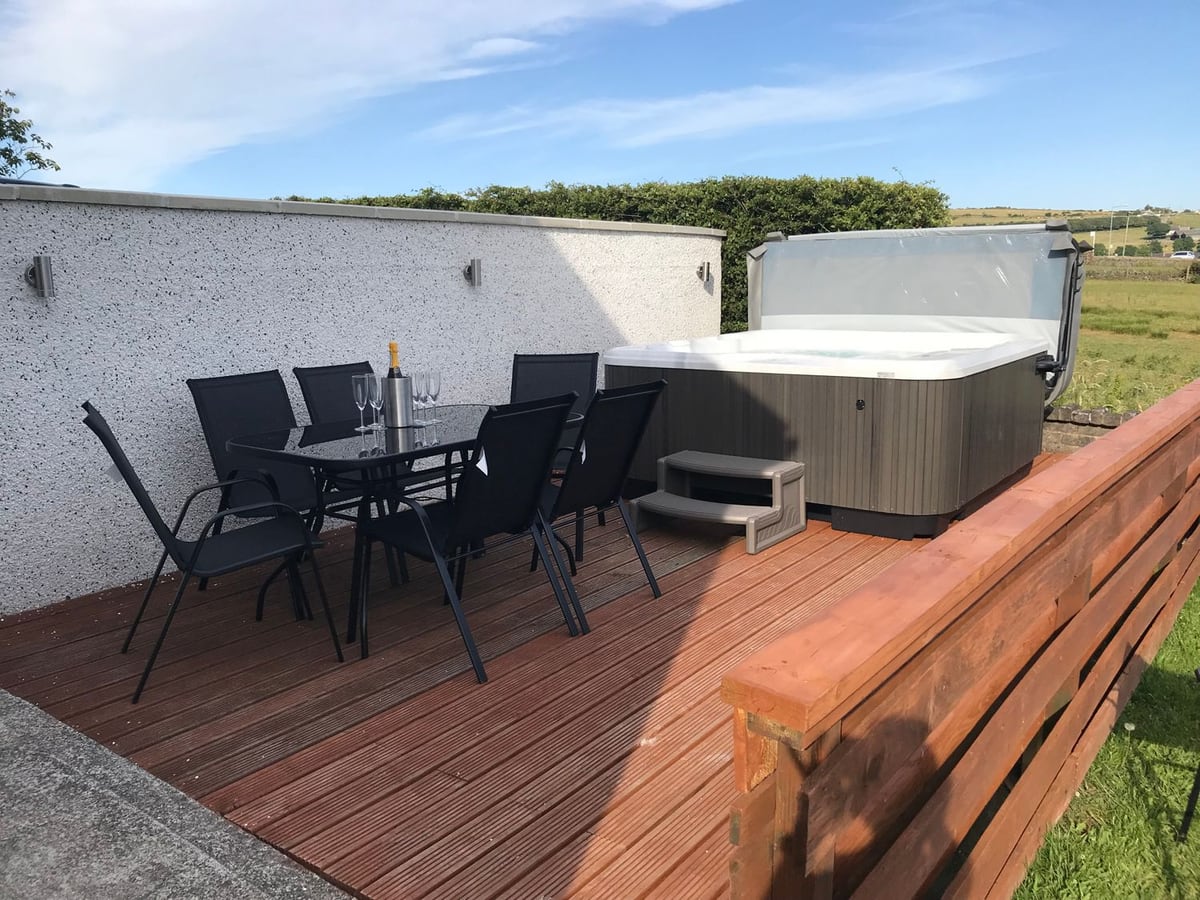 Rhos Helyg wooden deck with outdoor dining chairs and a hot tub beside a white wall