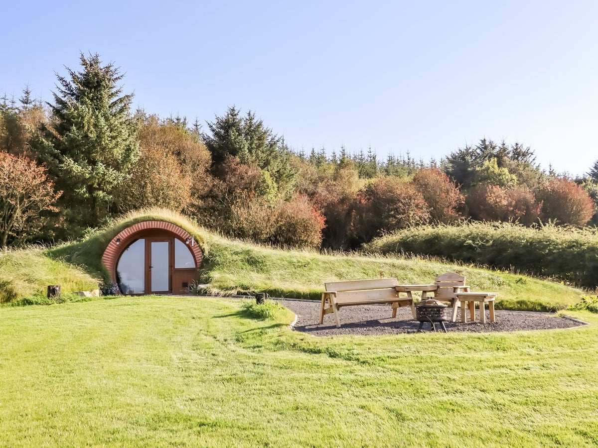 Rhosydd earth-covered pod with arched brick doorway, lawn and benches around a fire pit
