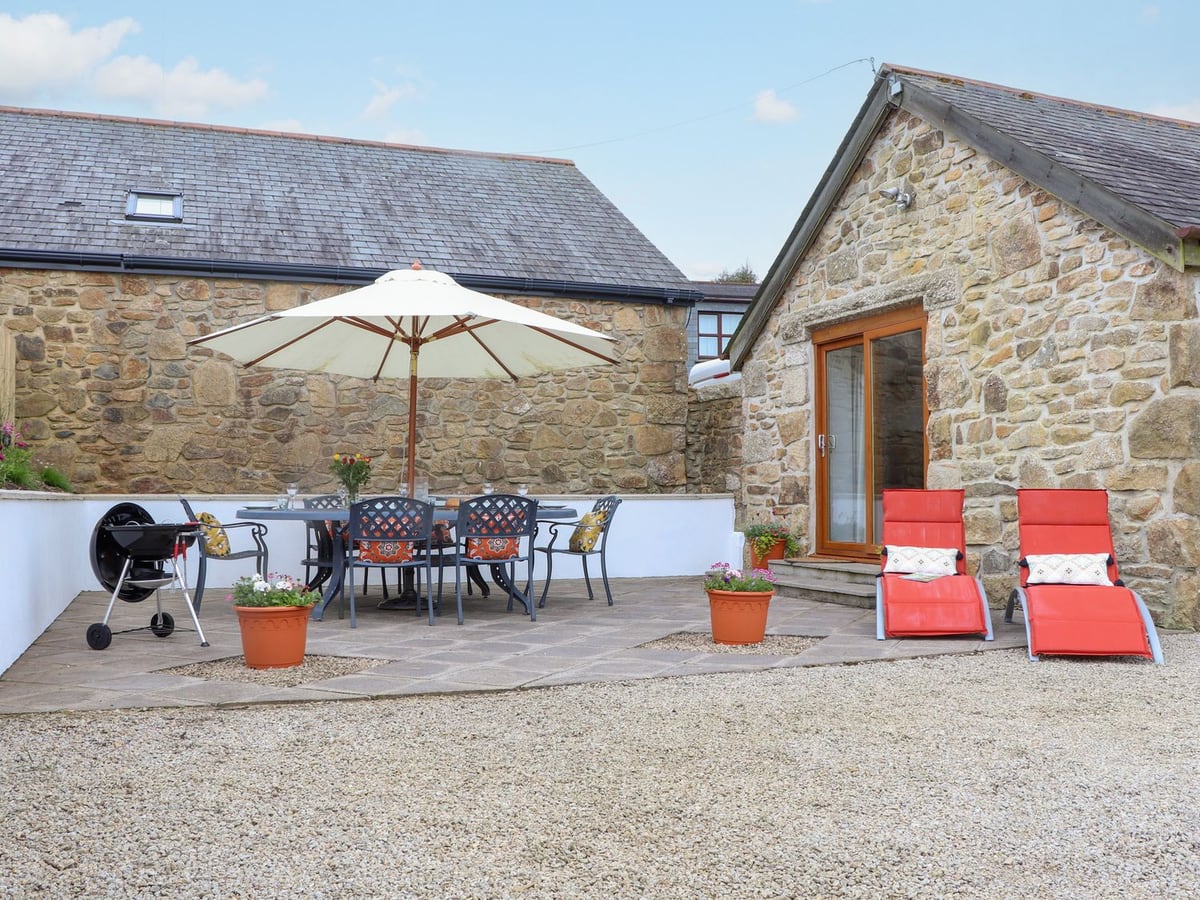 Stone exterior and gravel courtyard at Riviere Barton, with a patio table and red loungers