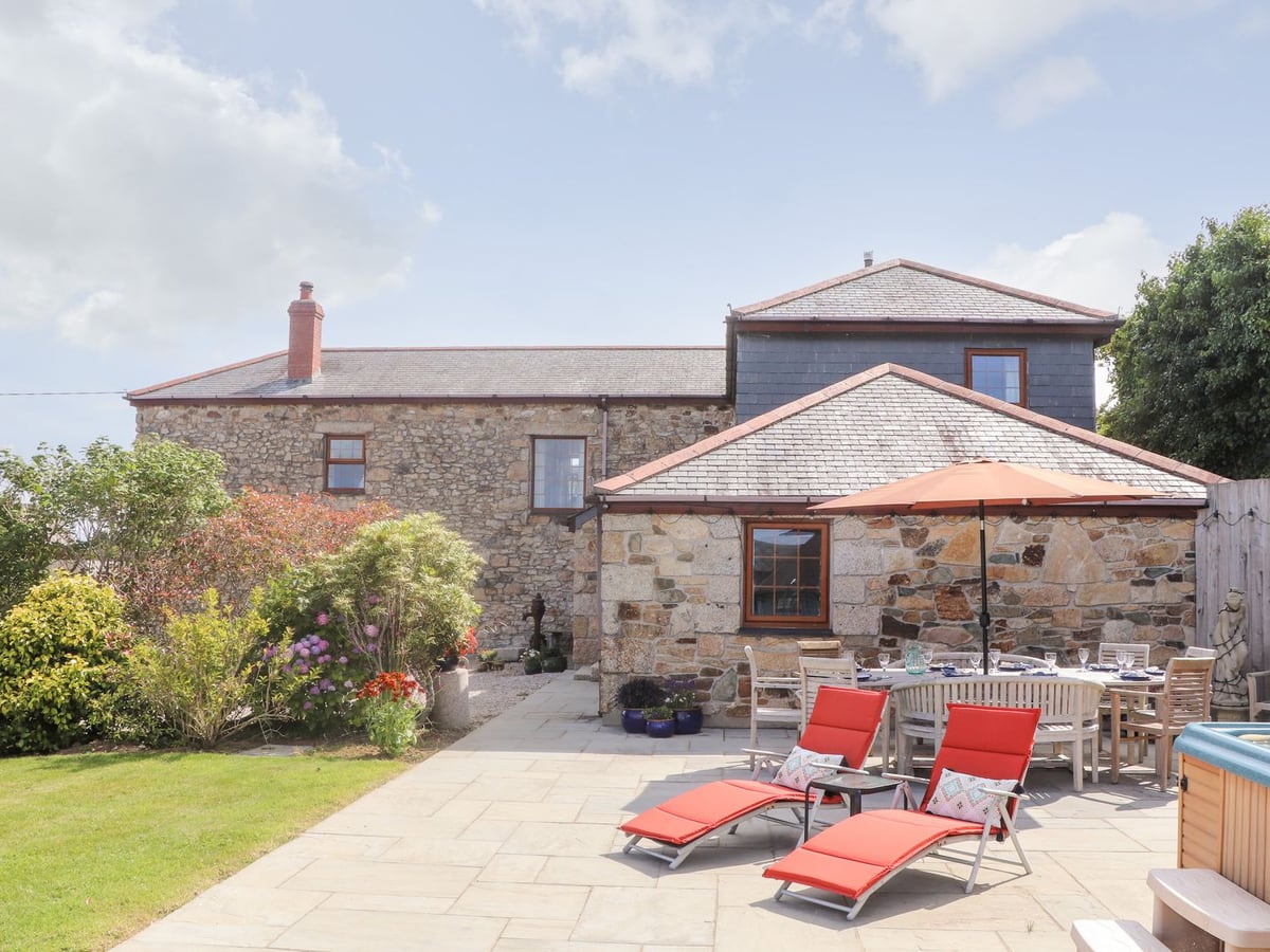 Riviere House stone exterior with a lawn, paved terrace, red loungers and outdoor dining table