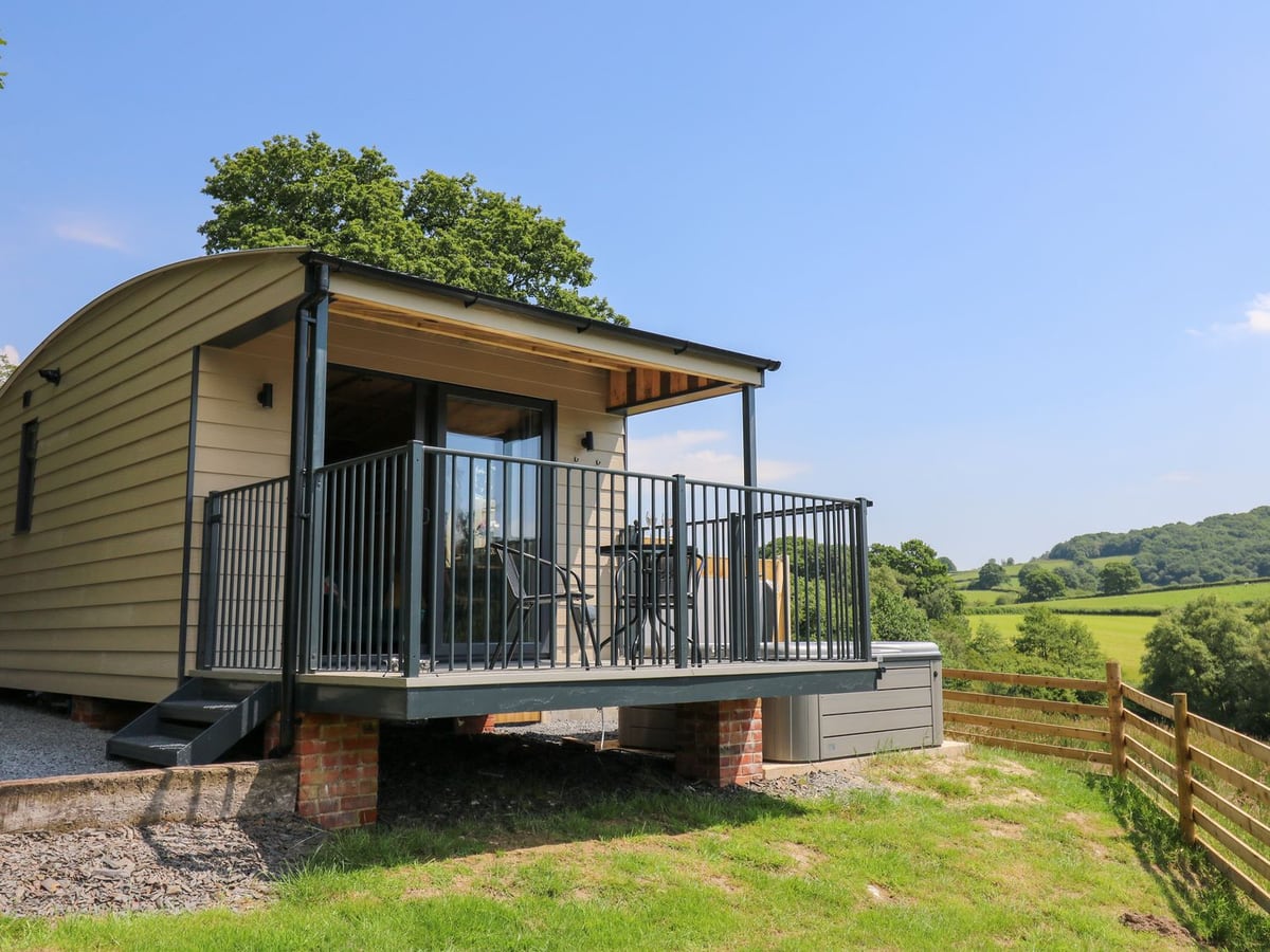 Rooster's Rest cabin with railed deck and chairs above a lawn, with fields and hills beyond