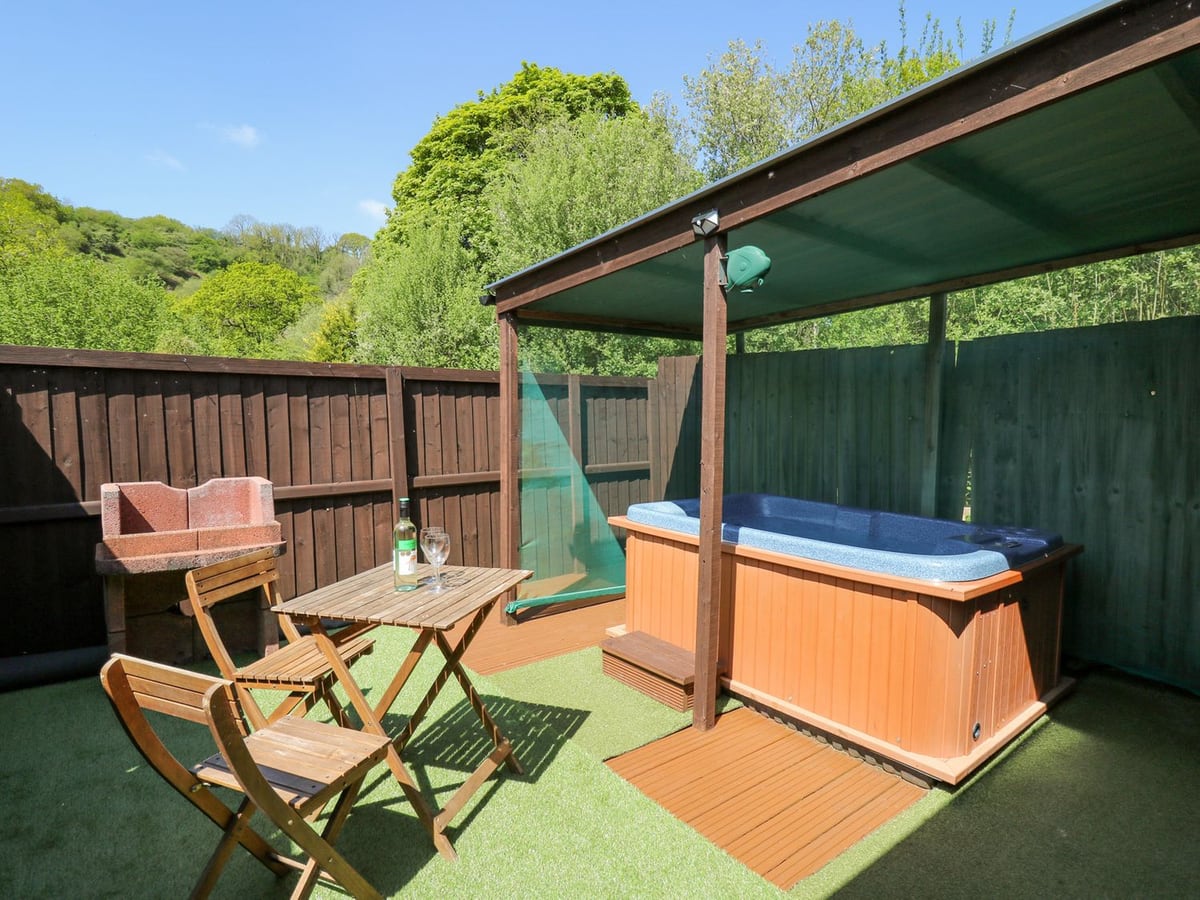 Hot tub under a canopy at Rose Cottage, with a wooden bistro set on artificial grass and wooden fences