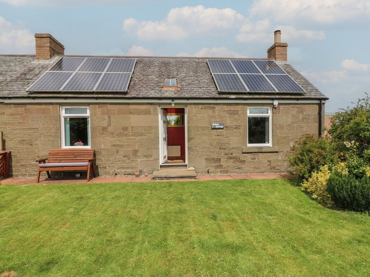 Rowan Cottage stone exterior with a red door, wooden bench and lawn in front of the house