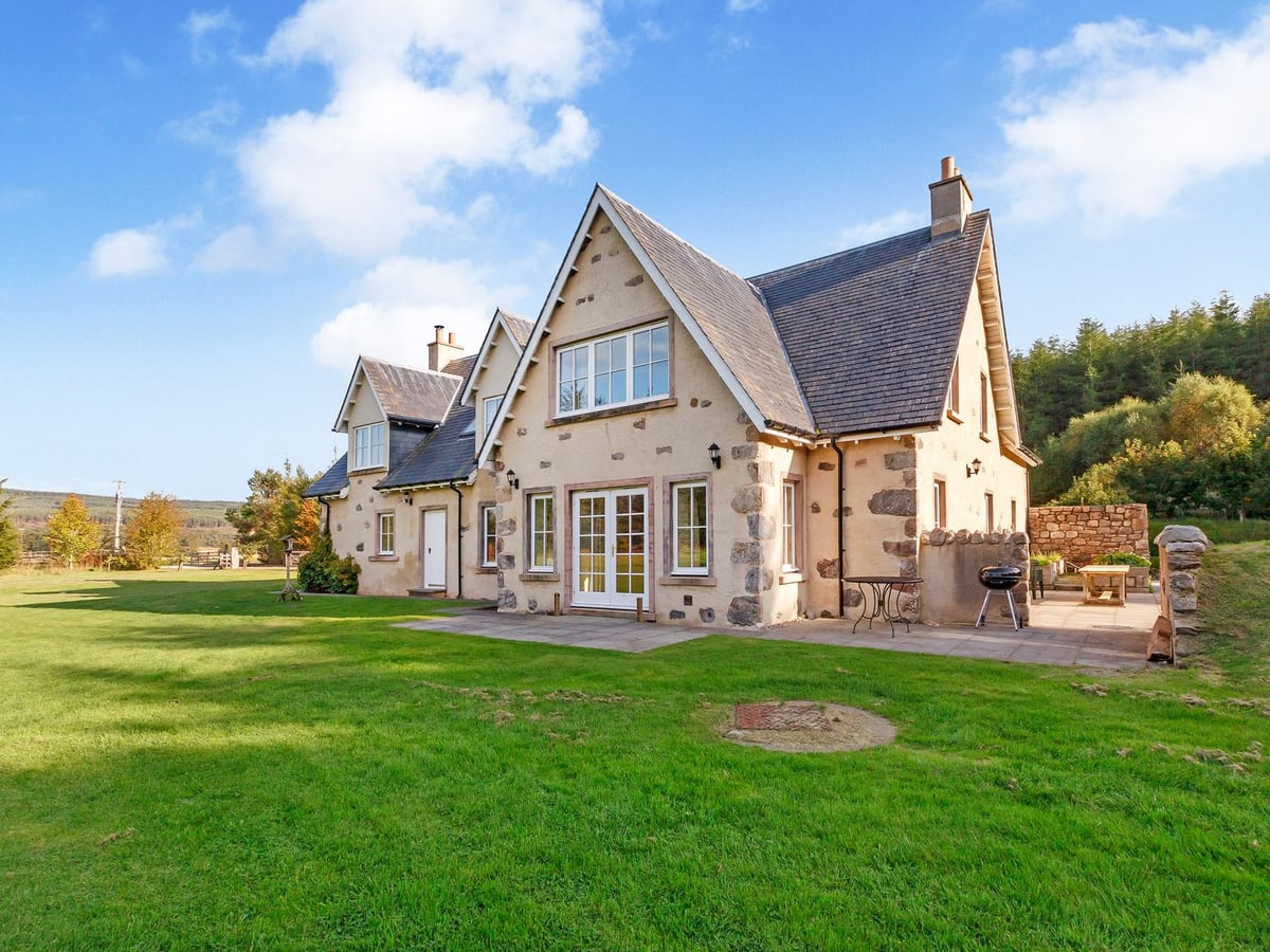 Rowan House with pale stone walls, a broad lawn and an outdoor seating terrace to one side