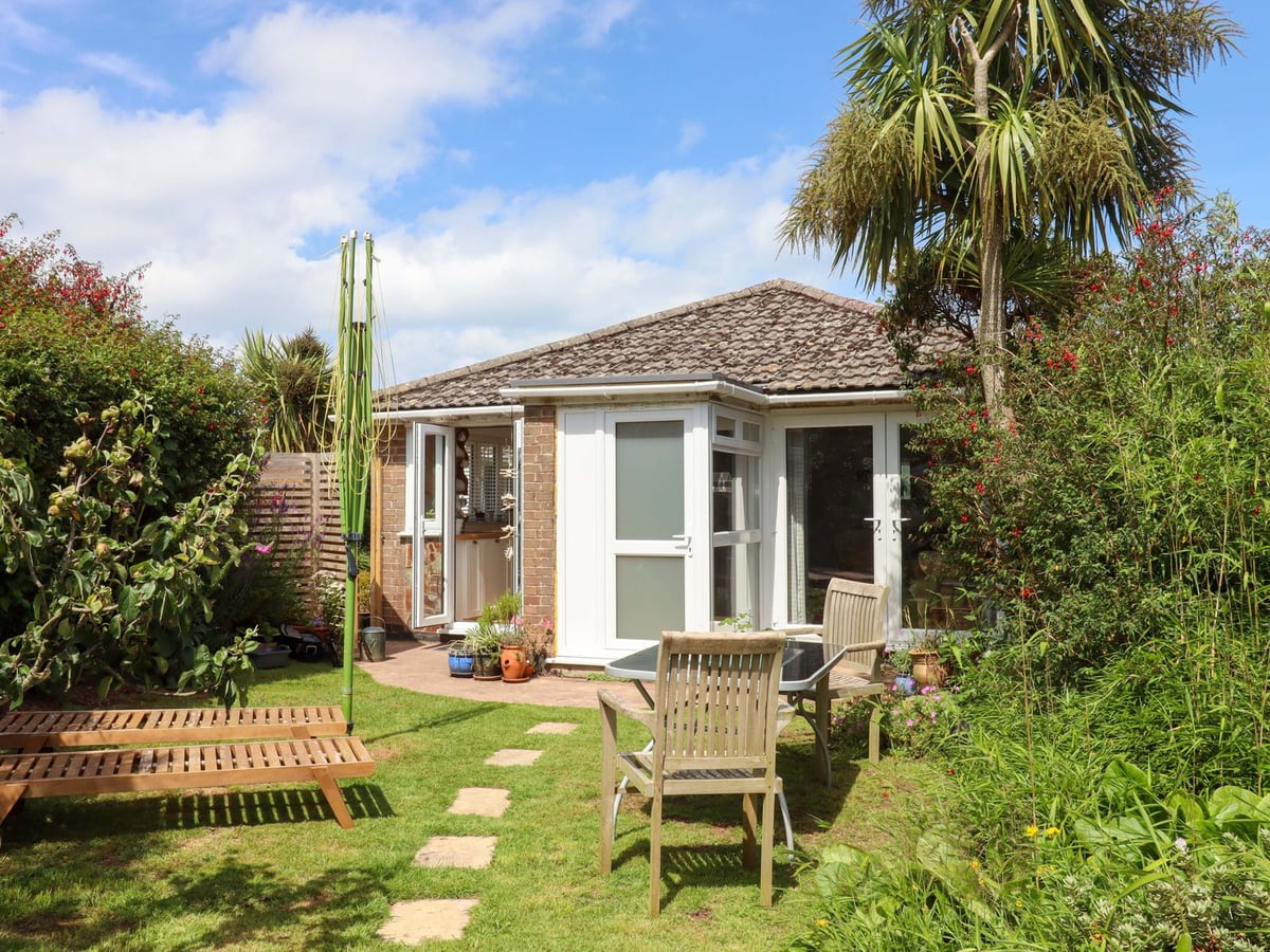 Bungalow with glazed garden doors, lawn and wooden outdoor furniture at Rowan