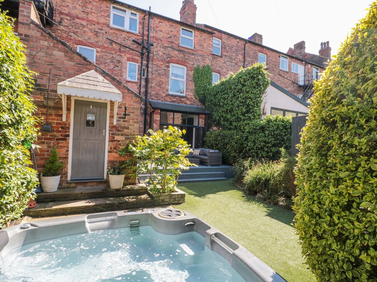 Garden patio with hot tub, lawn and brick house backdrop at Royal Victoria House