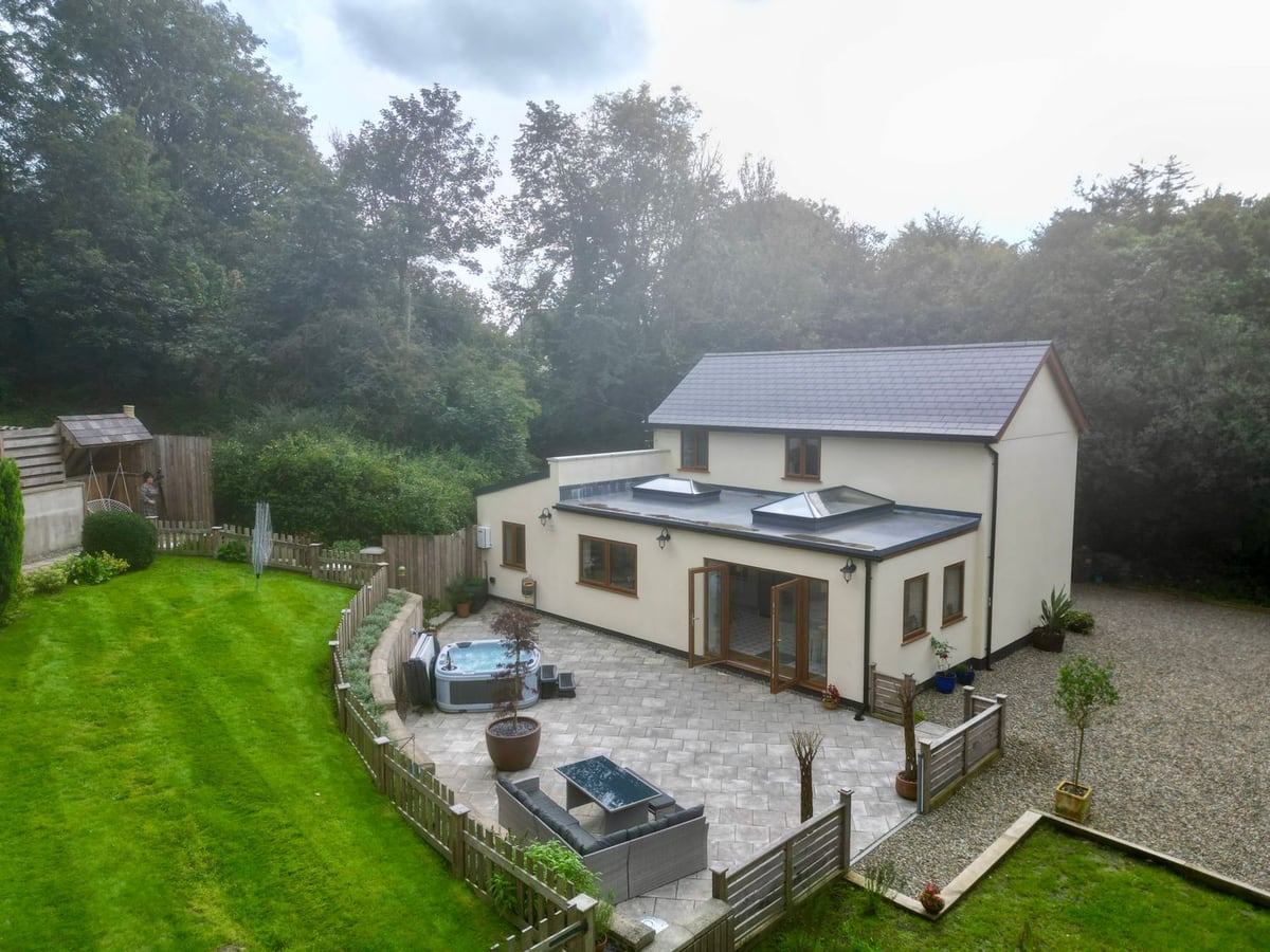 Rudbaxton Water cottage with a paved patio, hot tub and sofa set beside a fenced sloping lawn