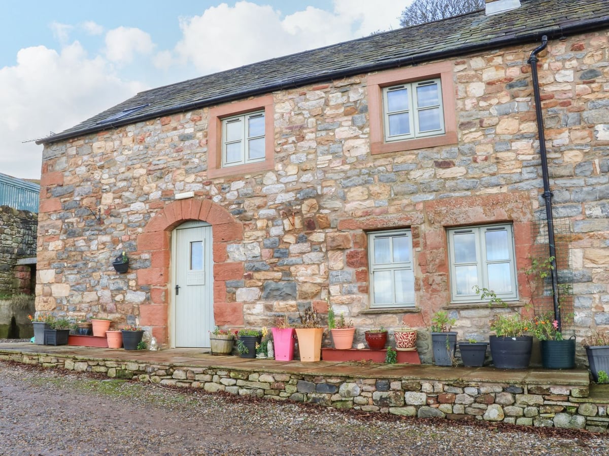 Stone frontage of Rum Bush Cottage with a pale door and colourful plant pots along the path
