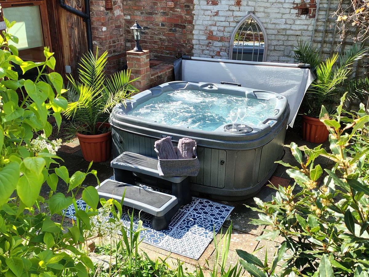 Runnymede hot tub surrounded by potted palms, with steps and a brick wall behind it