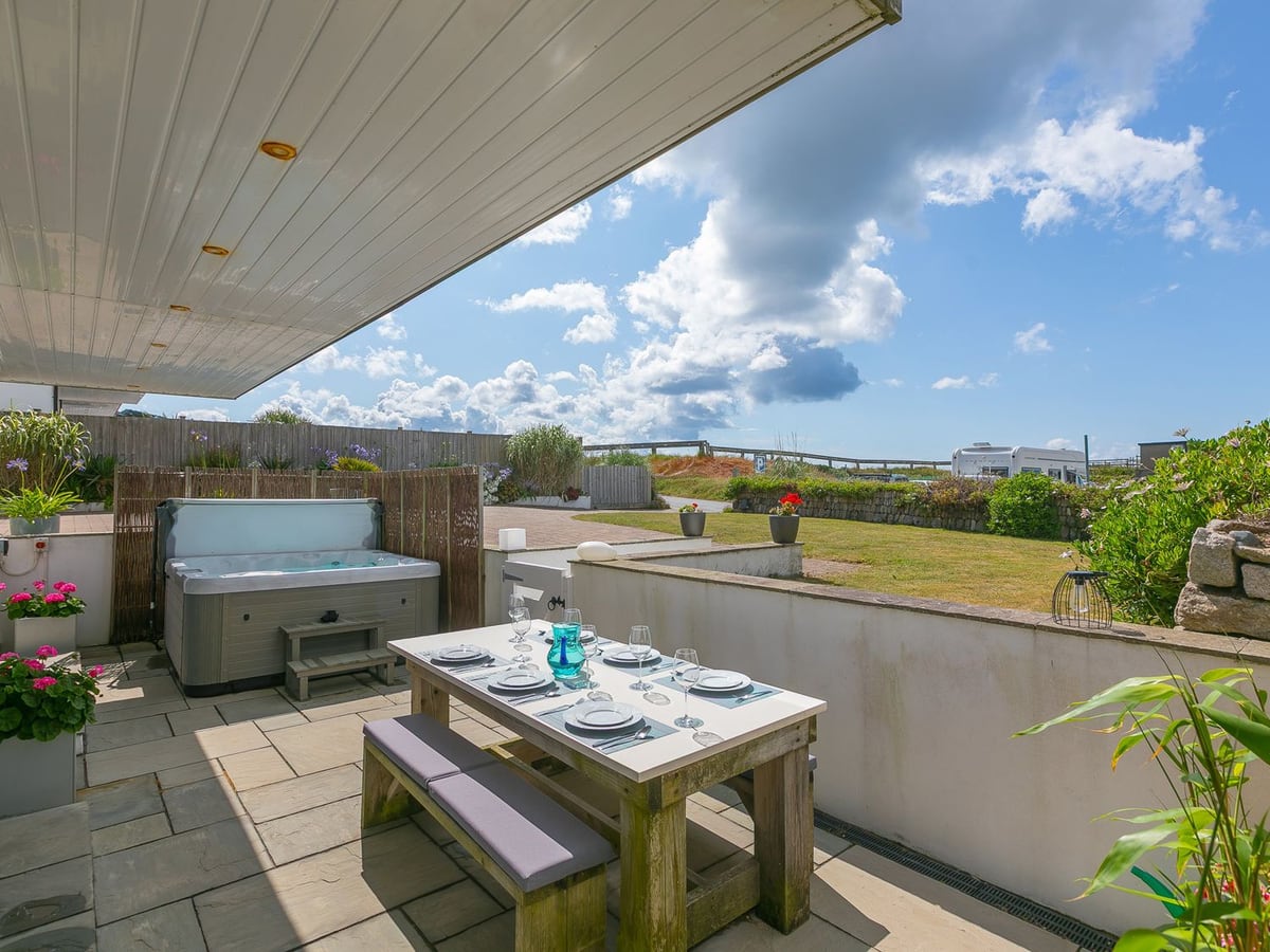 Hot tub and picnic table beneath Sandbanks' balcony, beside a lawn and low garden walls
