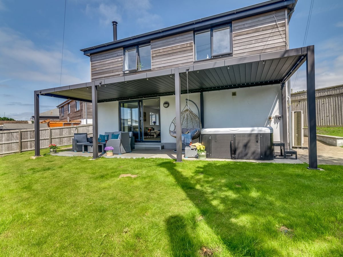 Sandy Cove's lawn and timber exterior, with a hot tub and seating beneath a broad patio canopy