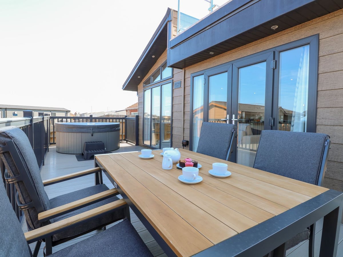 Dining table and chairs on the raised deck beside the hot tub at Sandy Snug in Bacton
