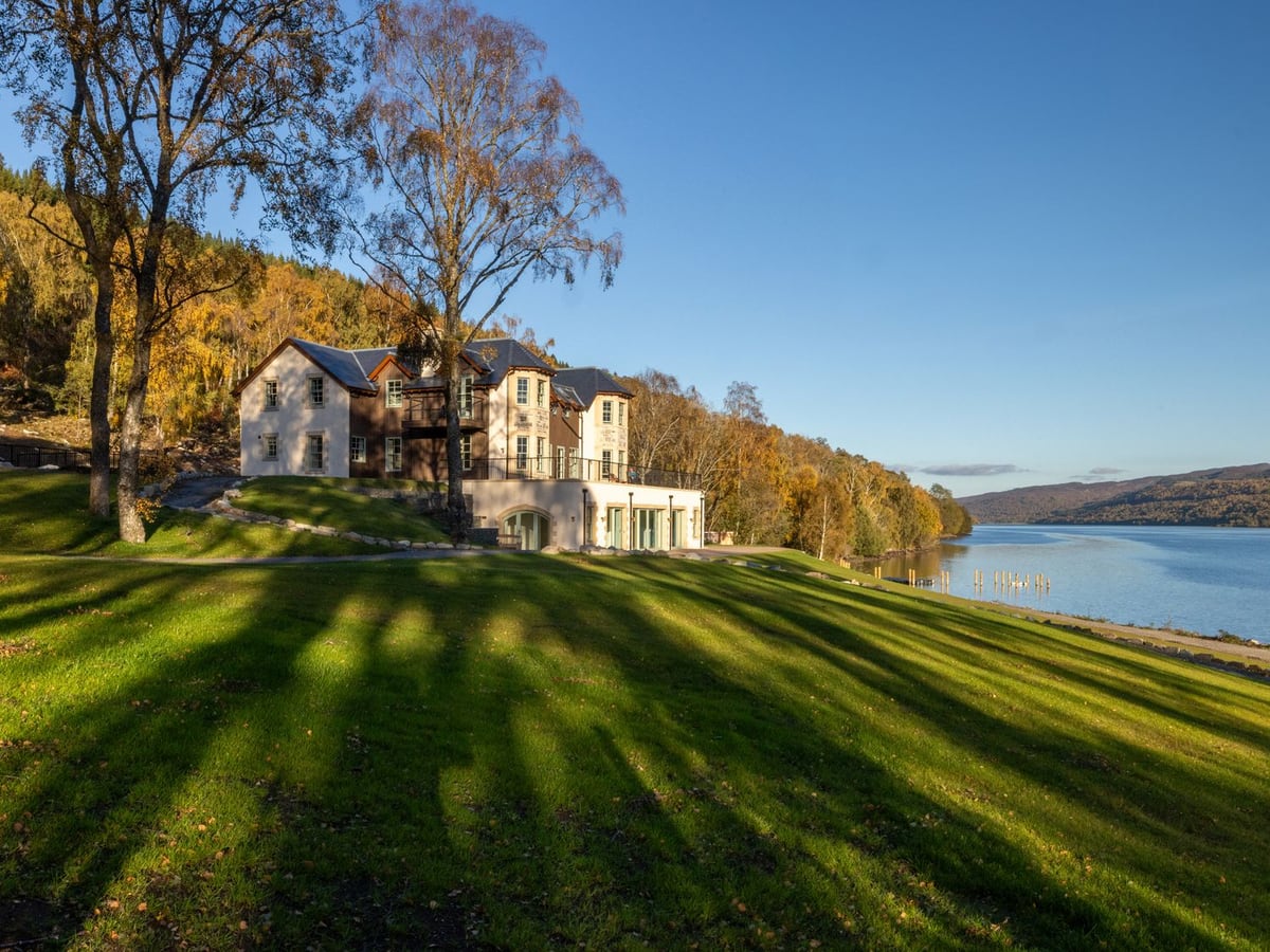 Schiehallion House above a sloping lawn beside the loch, with birch trees and wooded hills